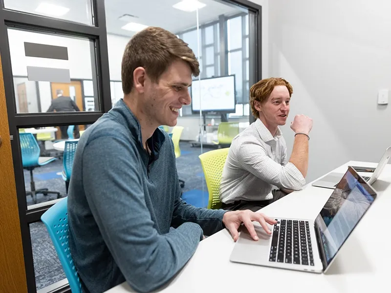 Two business major students work from their laptops.